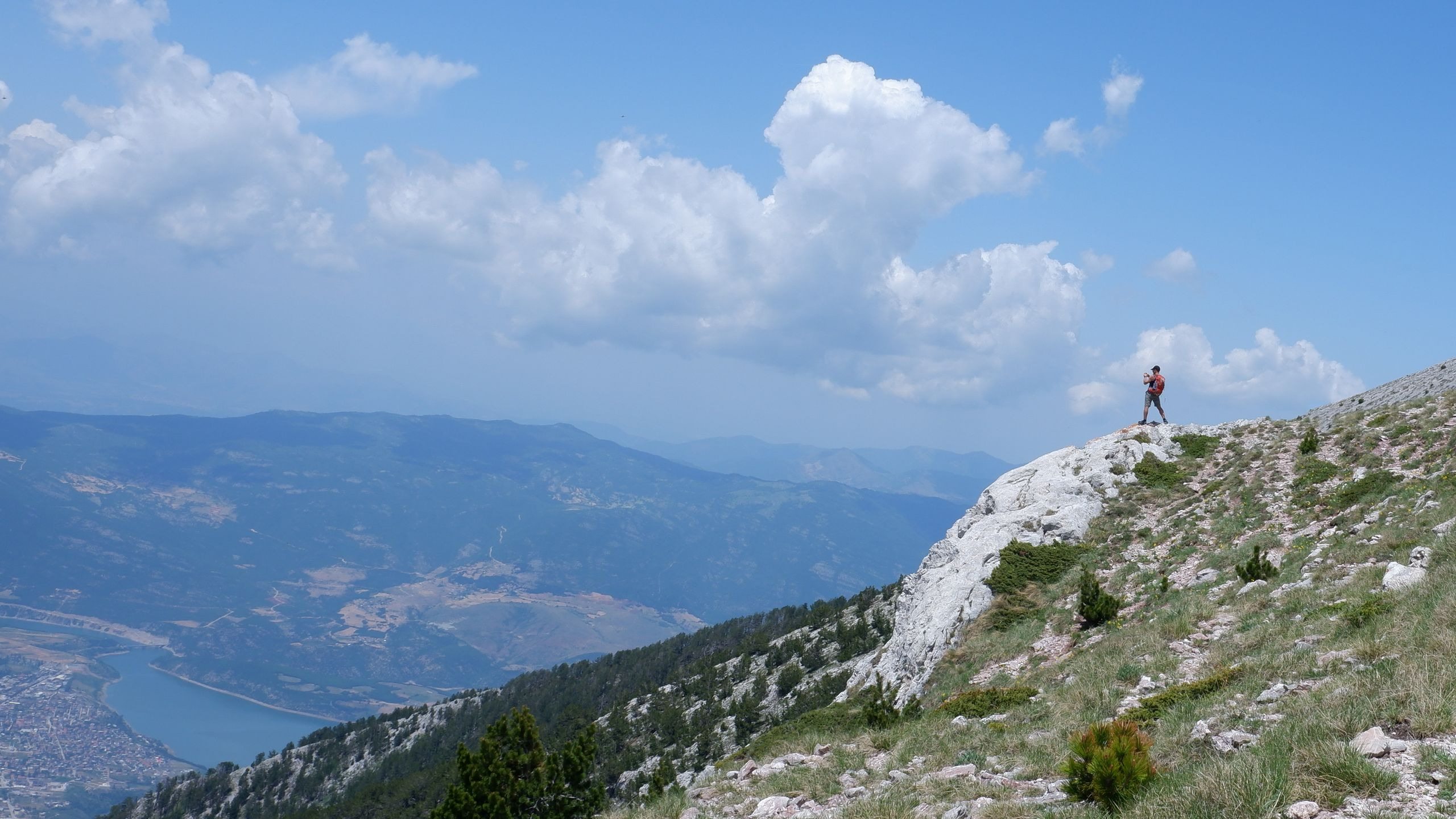 A trekker stands on a rocky ridge line, taking in a sweeping view of the valley far below.