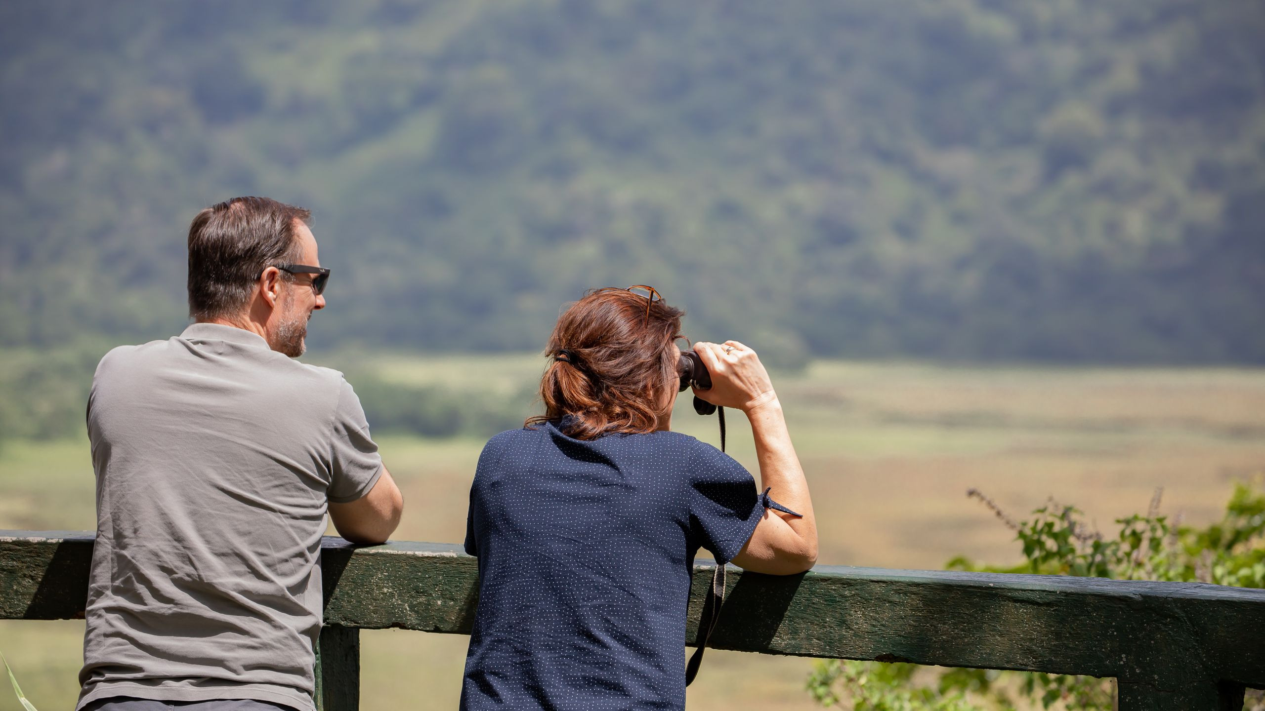 A couple shares a pair of binoculars while taking in a scenic savanna view together