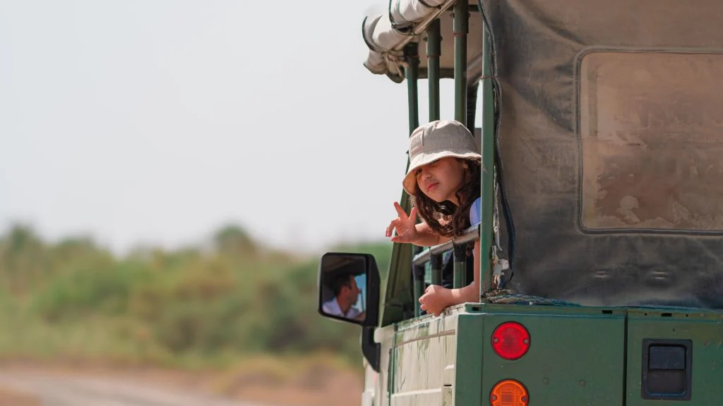 A young girl smiles while riding in an open-top safari vehicle through the wilderness