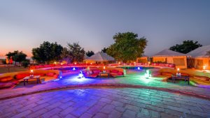 Elegant illuminated desert camp with vibrant seating and luxury tents at dusk